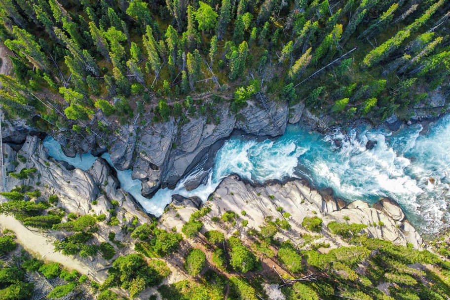 Luchtfoto recht van boven op een kolkende turkooizen rivier die tussen rotsen en naaldbos door een kloof stroomt in de Canadese Rockies