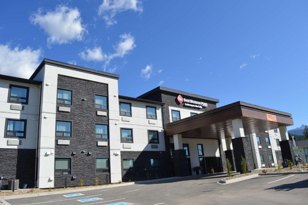 Gevel van een modern hotel in zwart en wit met een overdekte ingang en parkeerplaats, met bergen op de achtergrond onder een blauwe lucht