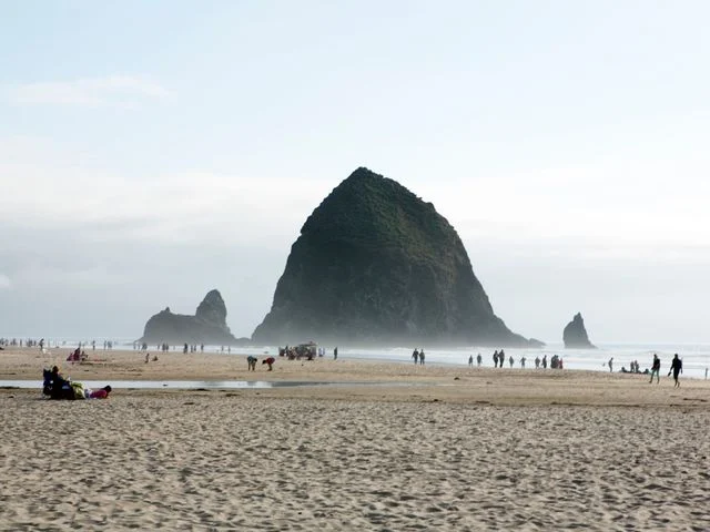 Wandelaars op het brede zandstrand van Cannon Beach met de rotsformatie Haystack Rock op de achtergrond in de mist