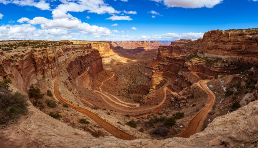 Een onverharde weg met scherpe haarspeldbochten daalt af door een rode canyon in Canyonlands National Park