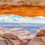 Beroemde rotsboog Mesa Arch met uitzicht op een uitgestrekt canyonlandschap, verlicht door de opkomende zon