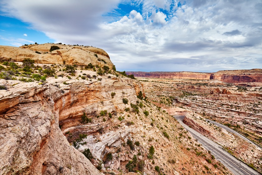 Een asfaltweg loopt langs de rand van een rotsachtige canyon met gelaagde rotswanden in Canyonlands National Park