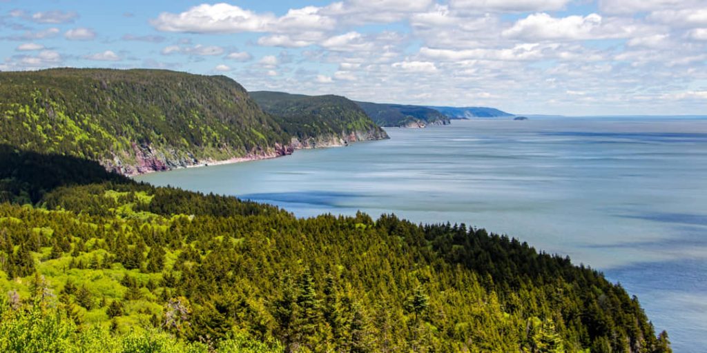 Glooiende beboste heuvels dalen af naar de zee in de Cape Breton Highlands onder een bewolkte lucht
