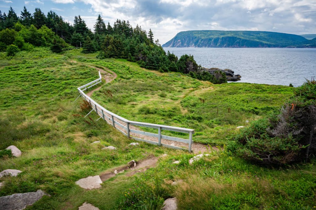 Houten vlonderpad met leuning slingert door groen grasland naar de kust met uitzicht op zee bij Cape Breton