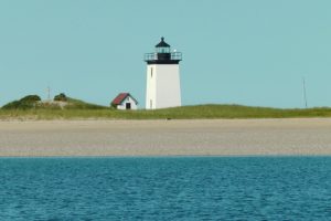 Witte vuurtoren met een huisje ernaast op een lage zandduin, gezien vanaf het water bij Cape Cod