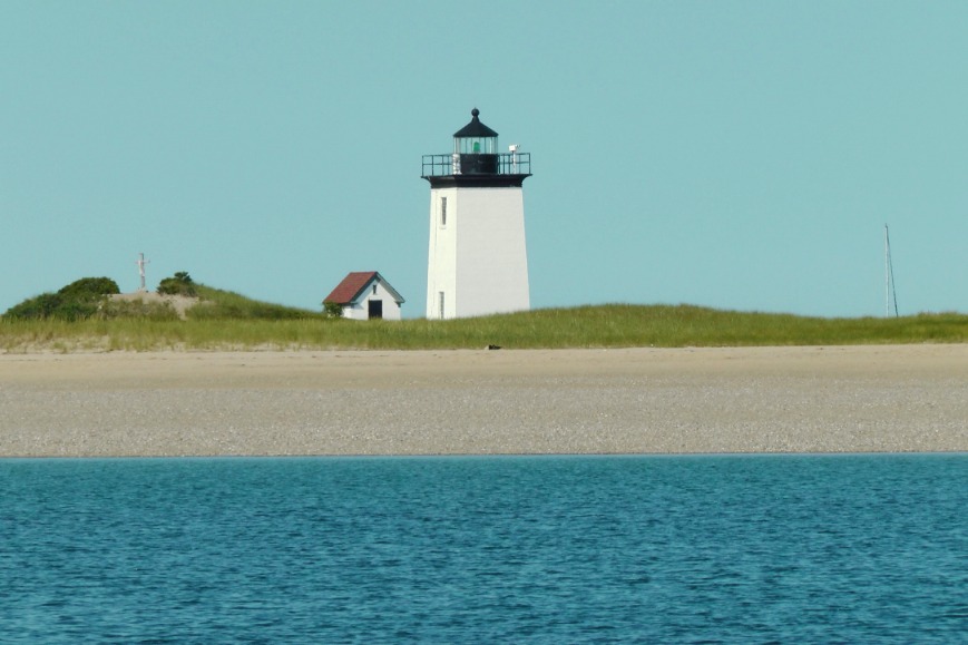 Witte vuurtoren met een huisje ernaast op een lage zandduin, gezien vanaf het water bij Cape Cod