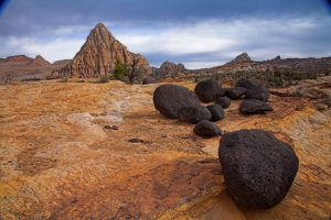 Ronde donkere basaltblokken liggen verspreid op een rode zandvlakte met de puntige rotsformatie Pectol's Pyramid op de achtergrond in Capitol Reef National Park