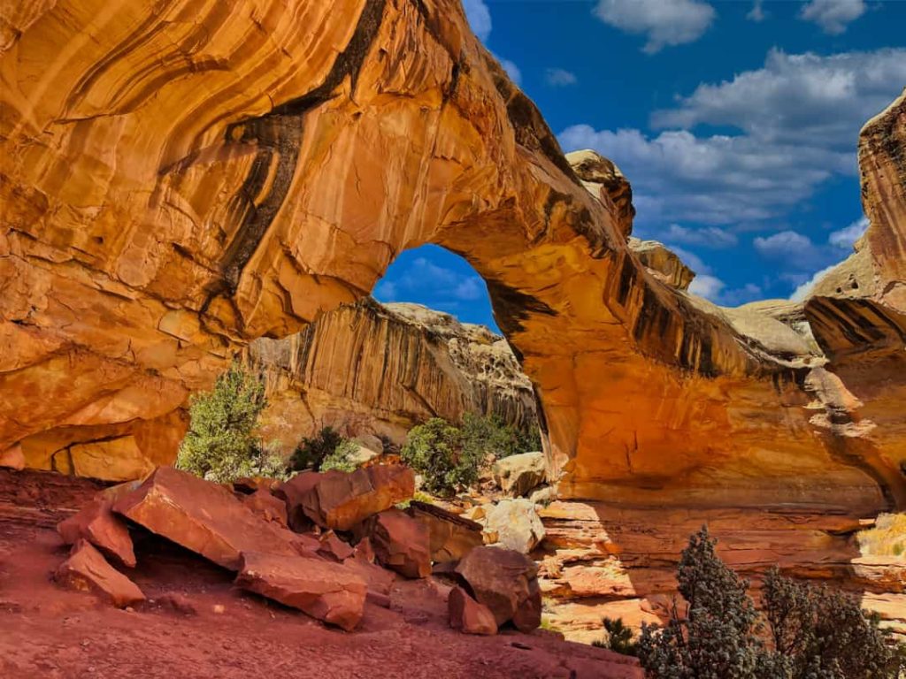 Grote natuurlijke rotsboog van gestreept oranje zandsteen met blauwe lucht erdoorheen in Capitol Reef National Park