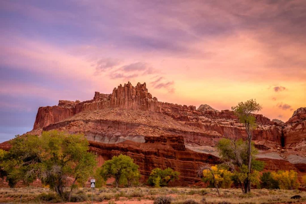 Getande rode rotsformatie steekt af tegen een paarsroze lucht bij zonsondergang in Capitol Reef National Park
