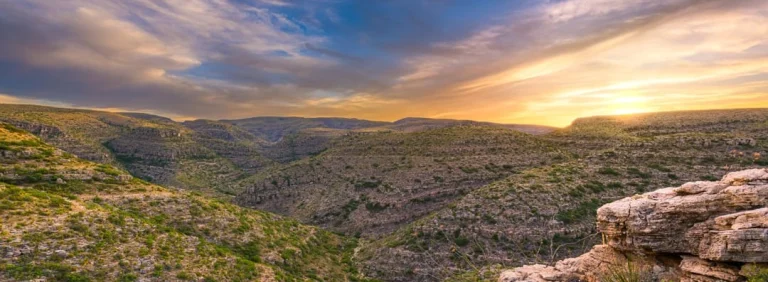 Breed panorama over golvende, met struikgewas begroeide heuvels van Carlsbad Caverns National Park onder een kleurrijke avondlucht