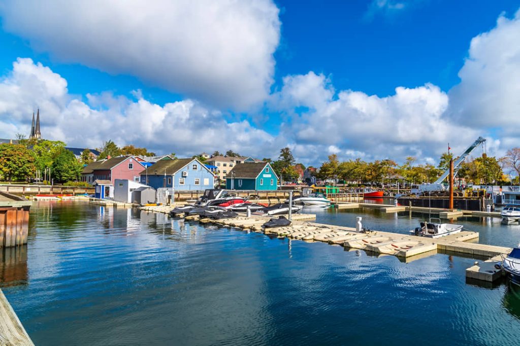 Boten liggen afgemeerd bij een jachthaven met kleurrijke huisjes en een kerktoren op de achtergrond in Charlottetown