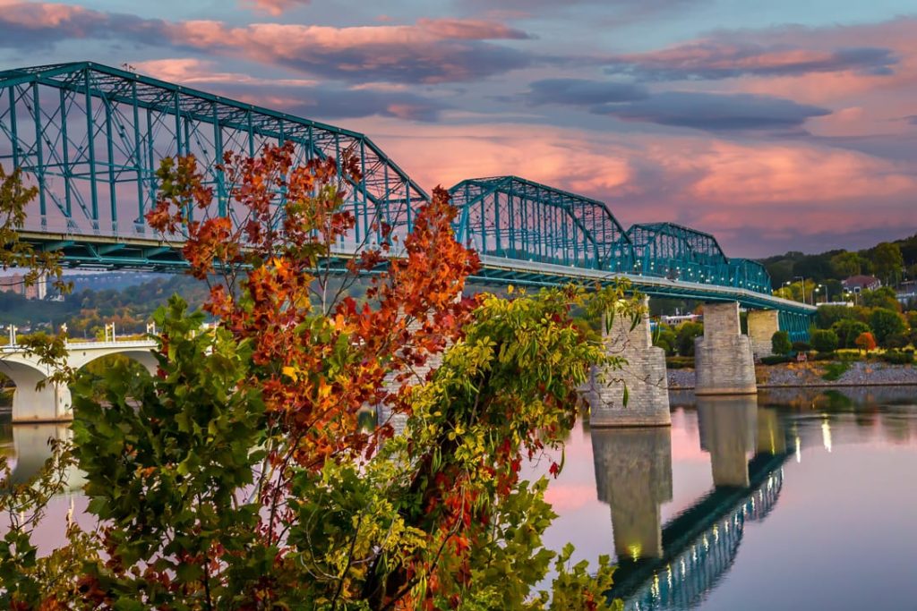 Groene stalen spoorbrug over de rivier in Chattanooga, met takken in herfstkleuren op de voorgrond