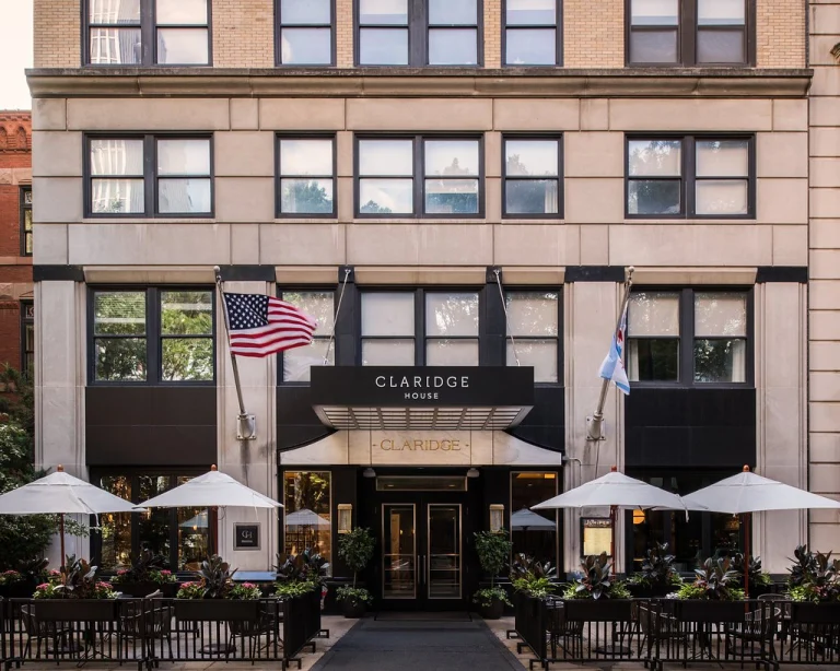 Lichte natuurstenen gevel van hotel Claridge House in Chicago met een terras vol witte parasols en Amerikaanse vlag