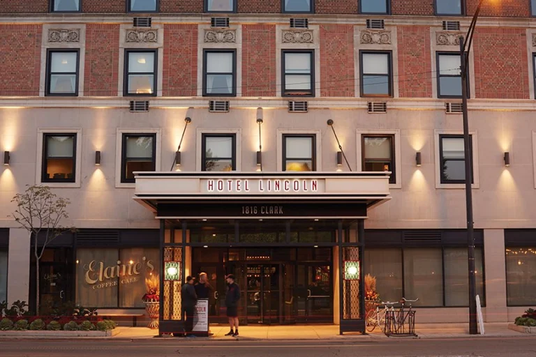 Bakstenen gevel van Hotel Lincoln in Chicago met verlichte luifel en ingang aan een straathoek bij avondlicht