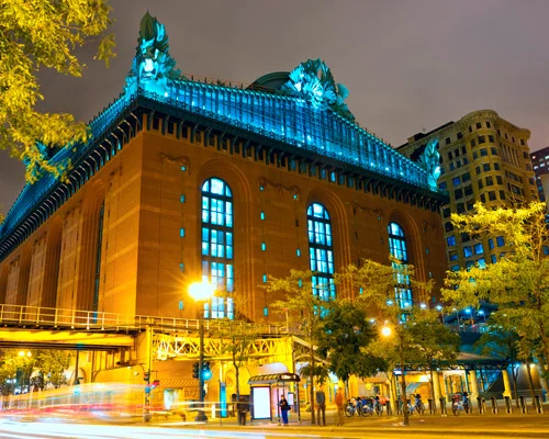 Monumentaal bibliotheekgebouw met booggewelfde ramen en sierlijke ornamenten, verlicht in blauw tegen de avondlucht in Chicago