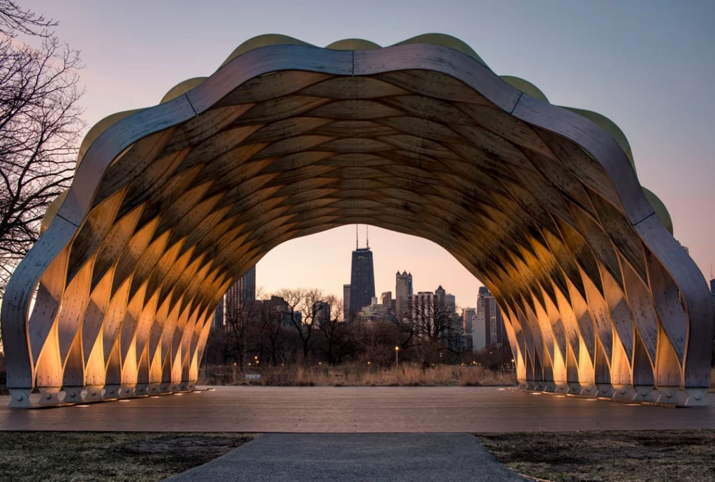 Golvend houten paviljoen met ronde bogen omlijst de skyline van Chicago inclusief de John Hancock-toren bij zonsondergang