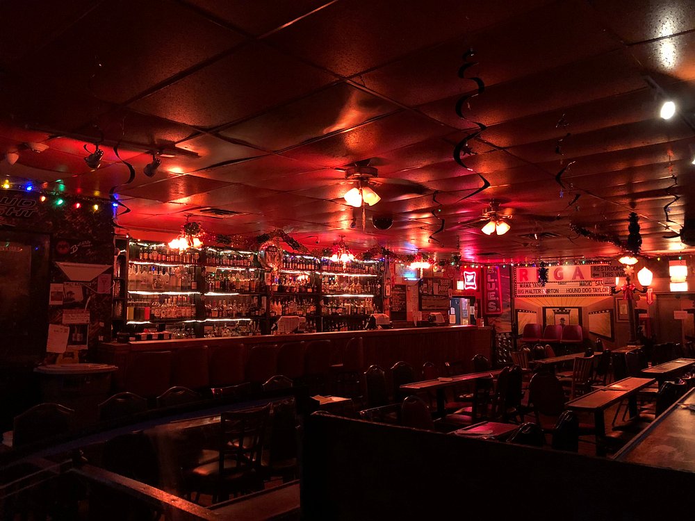 Interieur van een sfeervolle bluesbar met rood plafond en verlichting, een lange bar met flessen en lege houten tafels en stoelen
