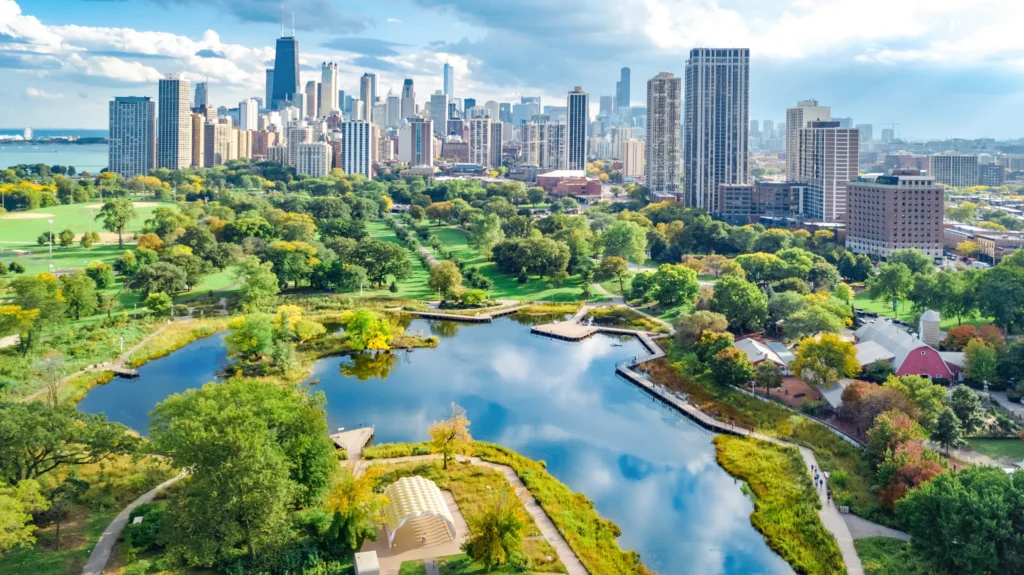 Luchtfoto van een groen park met een vijver en wandelpaden met op de achtergrond de wolkenkrabbers van Chicago