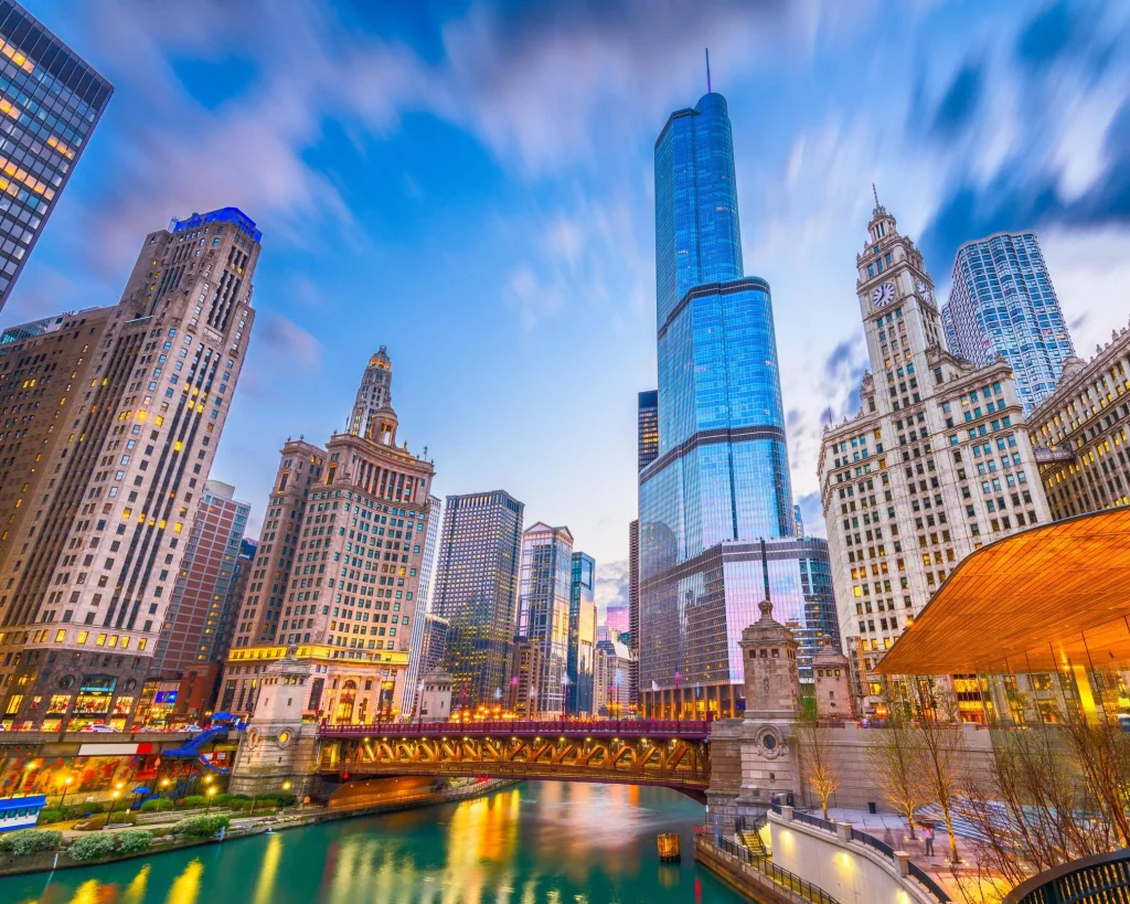 Wolkenkrabbers van Chicago aan weerszijden van de rivier met een verlichte brug en wazige wolken bij avondschemering