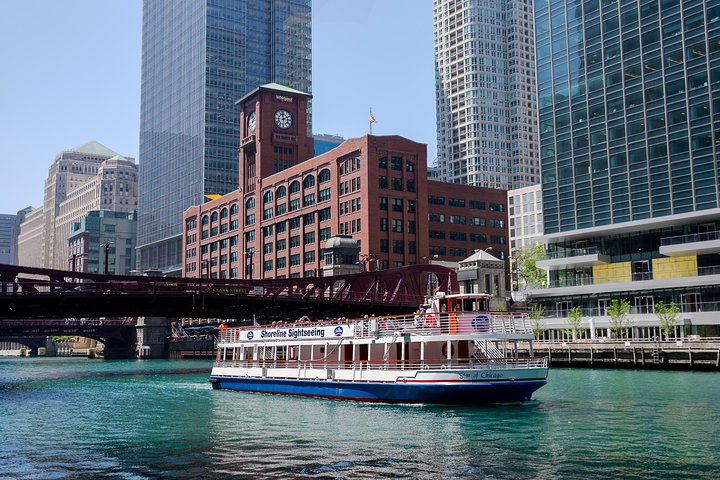 Sightseeingboot vaart onder een ophaalbrug door op de Chicago River langs een rood bakstenen gebouw met een klokkentoren en wolkenkrabbers op de achtergrond