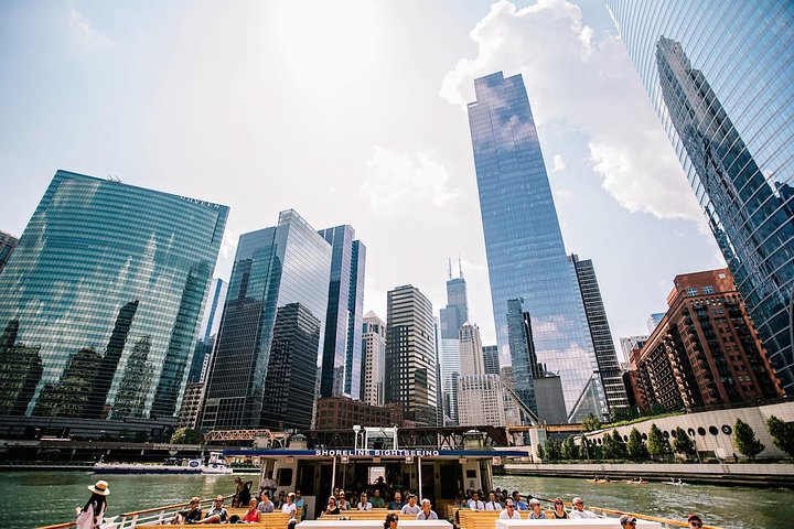 Volle rondvaartboot van Shoreline Sightseeing vaart over de rivier terwijl passagiers omhoog kijken naar de glazen torens en de Willis Tower op de achtergrond