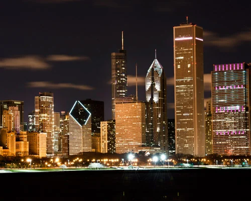 Verlichte wolkenkrabbers van Chicago waaronder een gebouw met een diamantvormige opening, gezien vanaf het meer bij nacht
