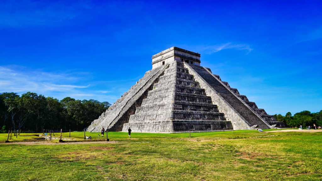 De getrapte stenen piramide van Kukulcán staat op een groen grasveld onder een heldere blauwe lucht in Chichén Itzá