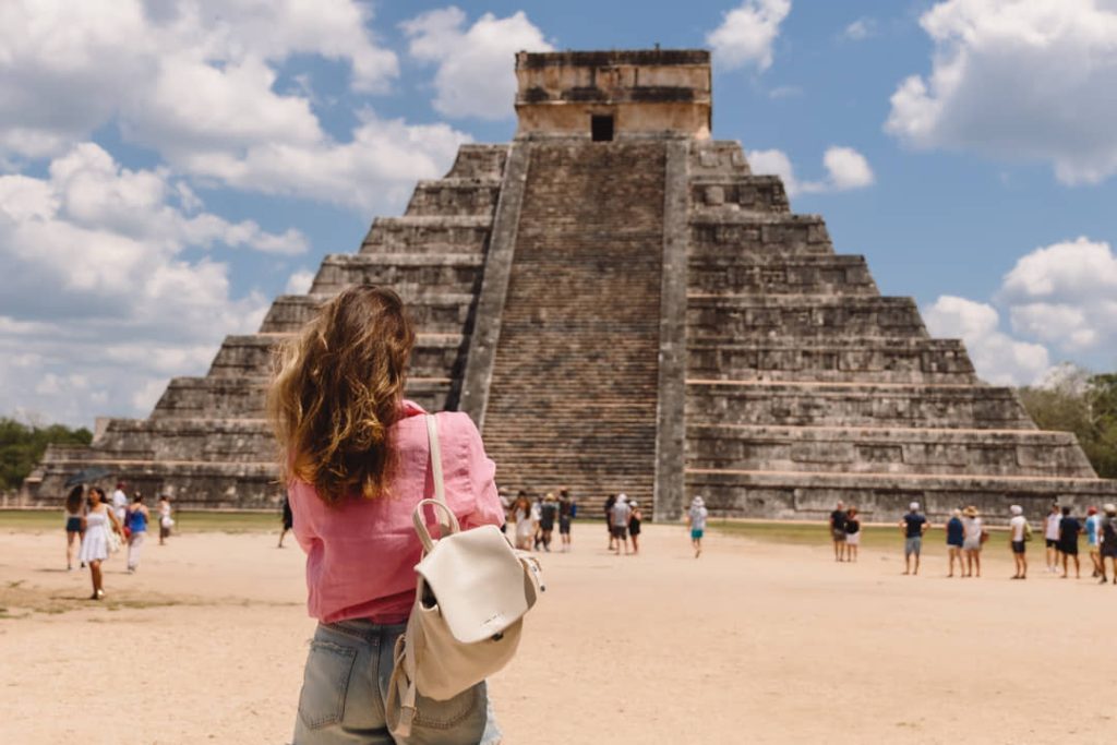 Een vrouw met rugzak staat met de rug naar de camera te kijken naar de getrapte piramide van Kukulcán in Chichén Itzá