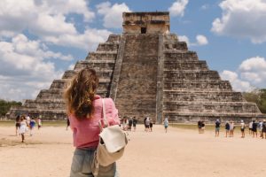 Een vrouw met rugzak staat met de rug naar de camera te kijken naar de getrapte piramide van Kukulcán in Chichén Itzá