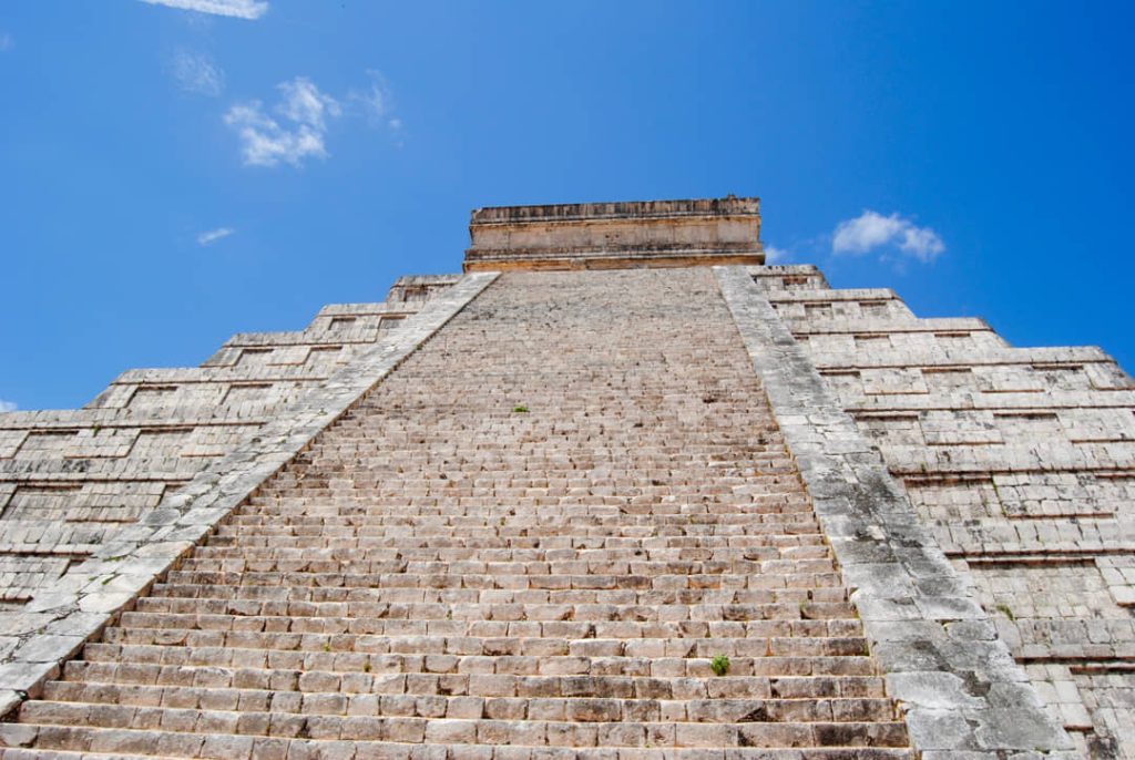 De steile stenen trap van de piramide van Kukulcán is van onderaf gefotografeerd tegen een blauwe lucht