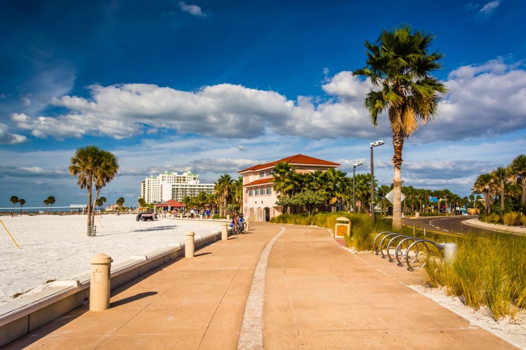 Breed betegeld pad langs het strand van Clearwater Beach met een roze gebouw met rode pannendak en hoge palmbomen