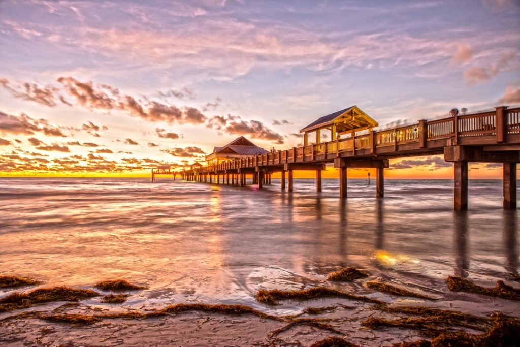 Houten pier met overkapping die ver de zee in steekt bij Clearwater Beach terwijl de zon net onder de horizon zakt