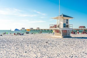 Wit zandstrand van Clearwater Beach met een reddingspost met nummer vier en een lange pier die de zee in steekt onder een blauwe lucht