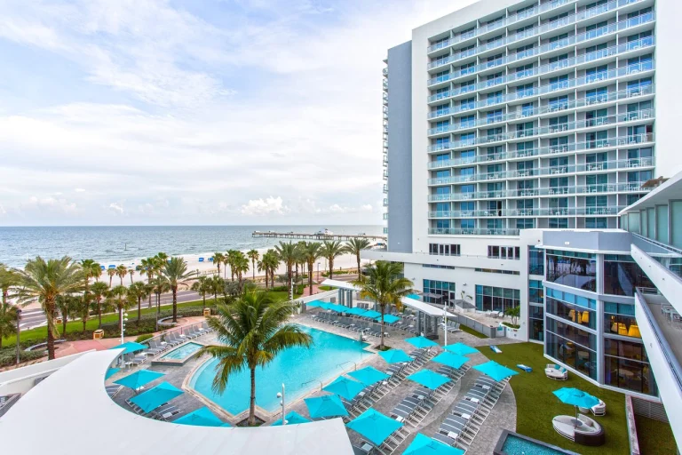 Uitzicht op het zwembad met blauwe parasols en ligstoelen bij het Wyndham Grand hotel in Clearwater, met het strand en de zee op de achtergrond
