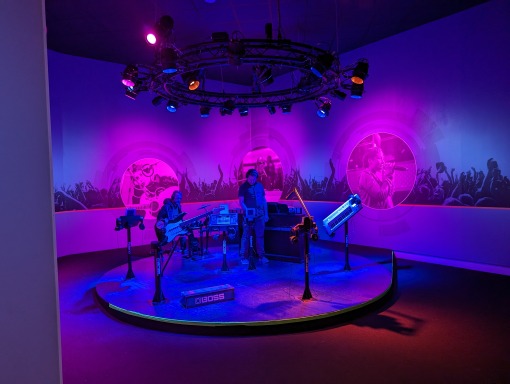 Rond podium met instrumenten en paarse verlichting omringd door schermen met concertbeelden in het GRAMMY Museum Mississippi