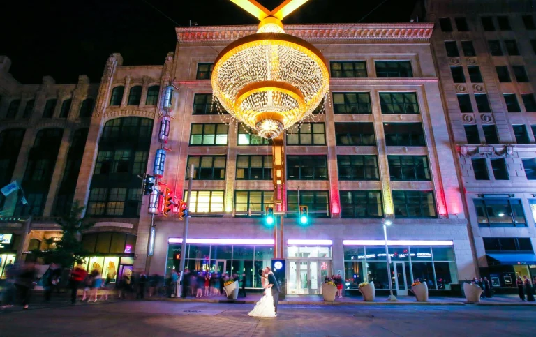 Een bruidspaar staat omhelsd onder de verlichte reuzenkroonluchter op Playhouse Square in Cleveland met historische gebouwen op de achtergrond