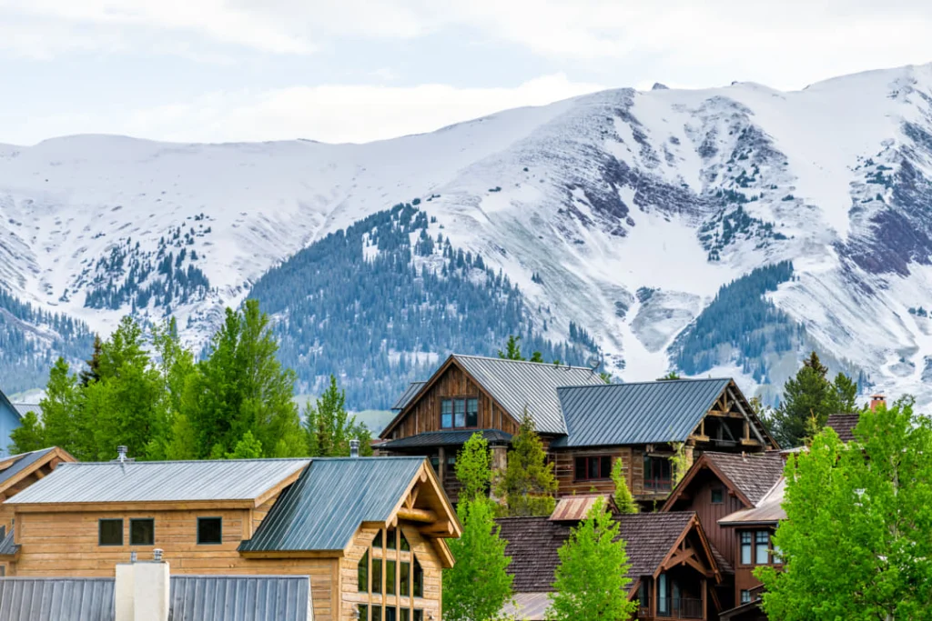Houten chalets met groene daken staan tussen naaldbomen voor een indrukwekkend besneeuwd bergmassief in Colorado