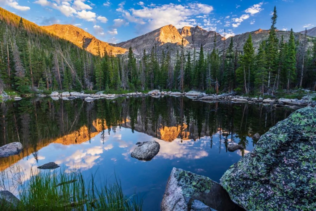 Rotsachtig bergmeer omgeven door dennenbos met de spiegeling van scherpe rotspieken bij zonsopgang in Colorado