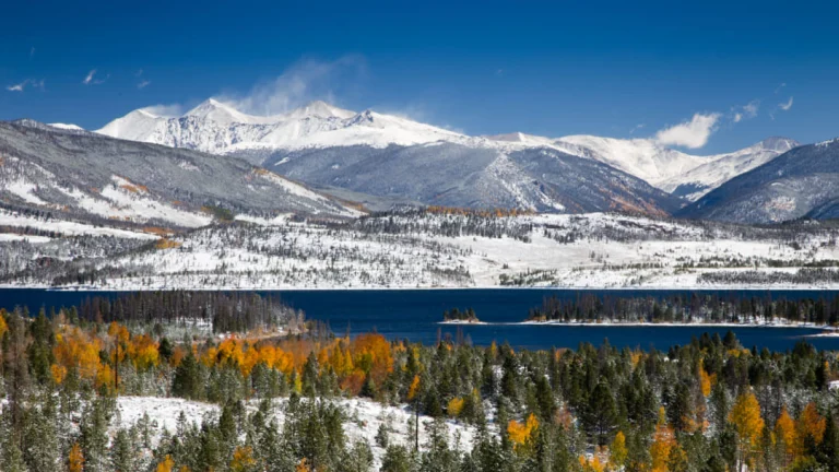 Blauw meer omgeven door besneeuwde bergen en bossen met goudgele en oranje herfstkleuren in Colorado