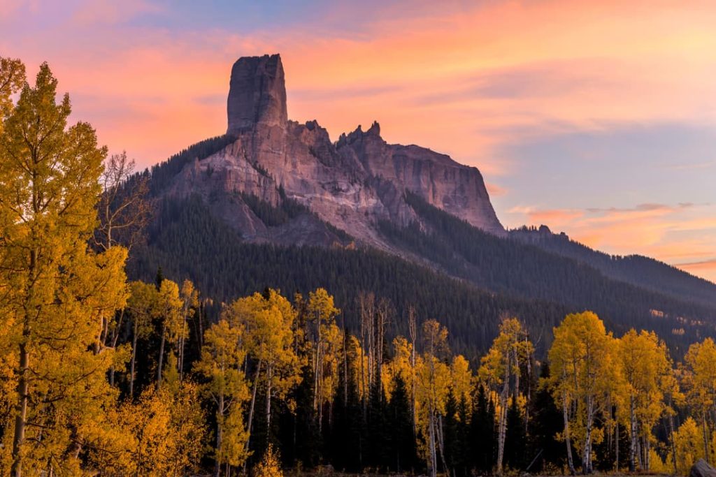 Getande rotstoren van Chimney Rock kleurt roze in de avondzon boven een vallei vol gele herfstbomen in Colorado