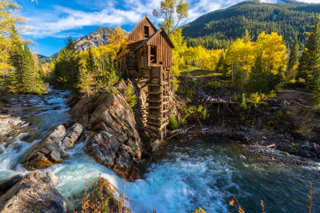 Houten Crystal Mill gebouwd op een rotsformatie boven een stromende rivier, omgeven door herfstkleurig bos
