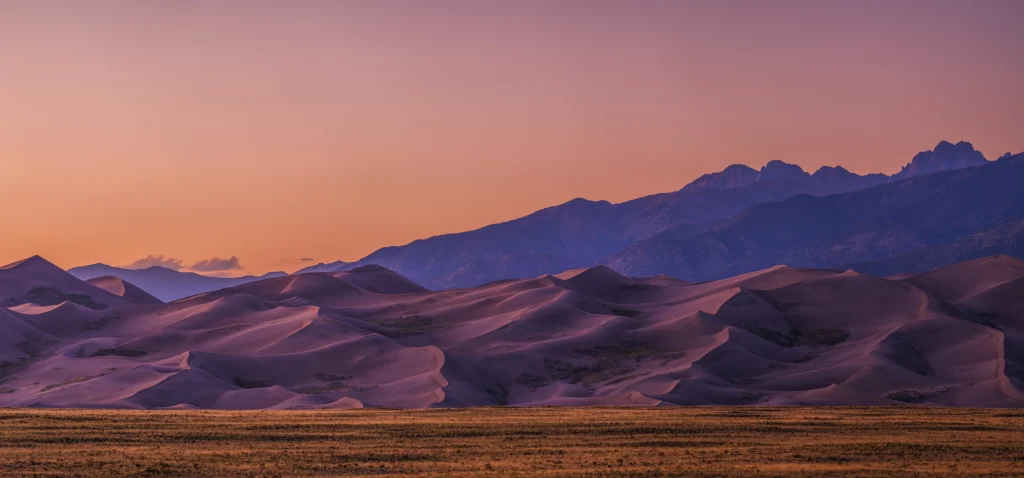 Hoge zandduinen met bergen op de achtergrond in warm licht bij zonsondergang in Great Sand Dunes National Park in Colorado