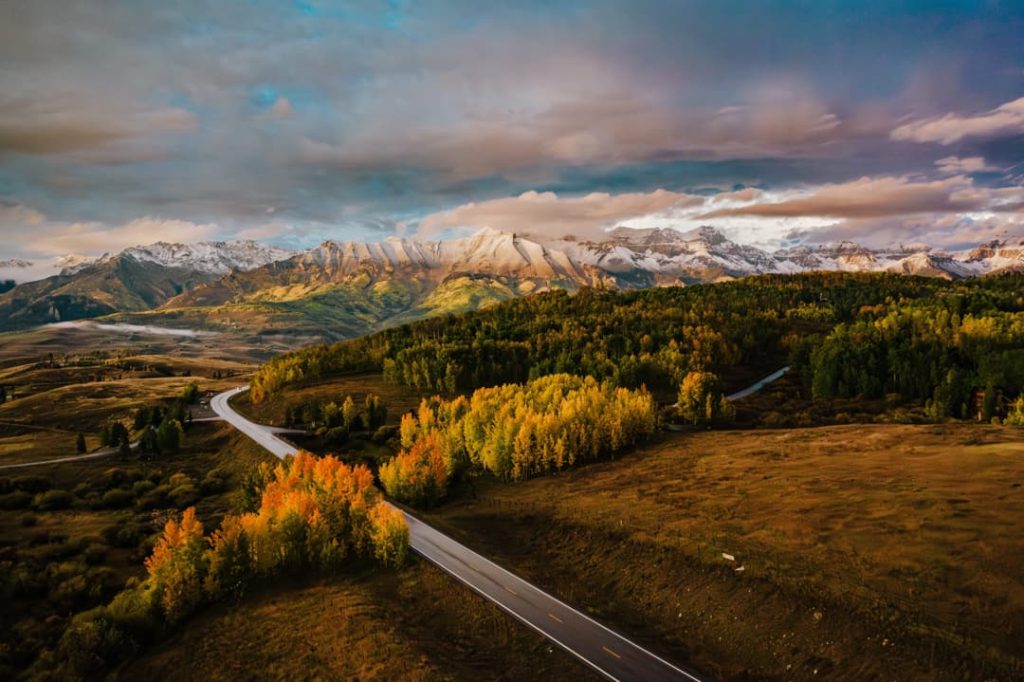 Luchtfoto van een weg die kronkelt door een herfstlandschap met goudgele bomen en besneeuwde bergen op de achtergrond in Colorado