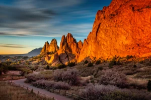 Hoge oranjerode rotspieken van Garden of the Gods worden verlicht door de laagstaande zon terwijl een pad tussen struikgewas naar de formaties leidt