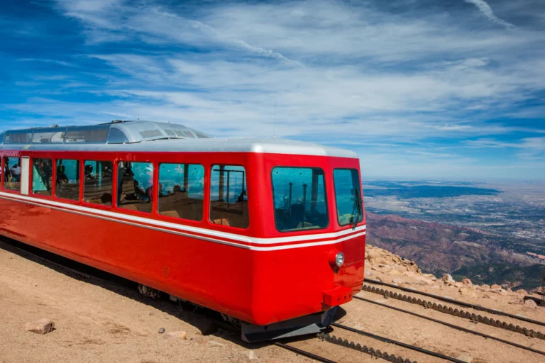 Rood met wit treinstel van de tandradbaan staat op de rails bij de top van Pikes Peak met een wijds uitzicht over de omliggende bergen