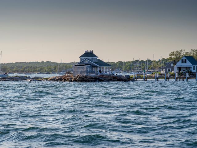 Grijs huis met veranda gebouwd op een rotsachtig eiland omringd door zeilboten in een jachthaven aan de kust van Connecticut