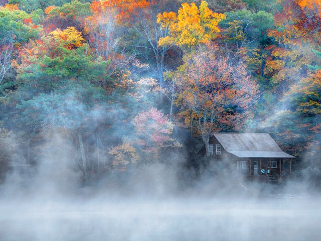 Houten hut tussen kleurrijke herfstbomen aan een meer met opstijgende mist boven het water in Connecticut