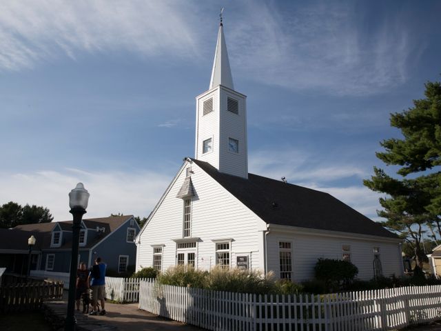 Witte houten kerk met een hoge spits en wit hekwerk waar een gezin voor staat te kijken in Connecticut