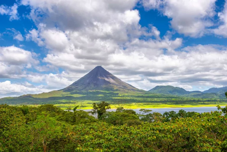 Uitzicht op de kegelvormige Arenal vulkaan in Costa Rica met een meer en weelderige jungle op de voorgrond onder een bewolkte lucht