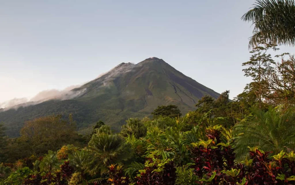 De kegelvormige Arenal-vulkaan in Costa Rica steekt boven groene jungle uit met wat wolken tegen de hellingen